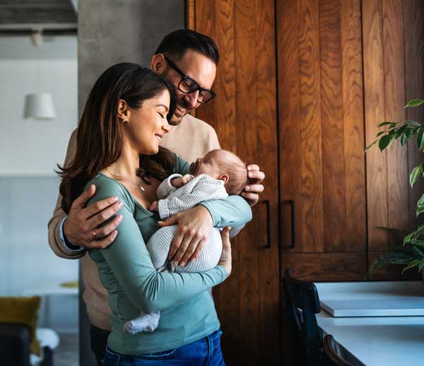 Parents with Infant standing in front of a window smiling