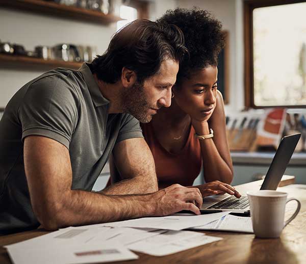 UtilityShield Home Protection, couple in their kitchen looking at a computer with a pile of bills