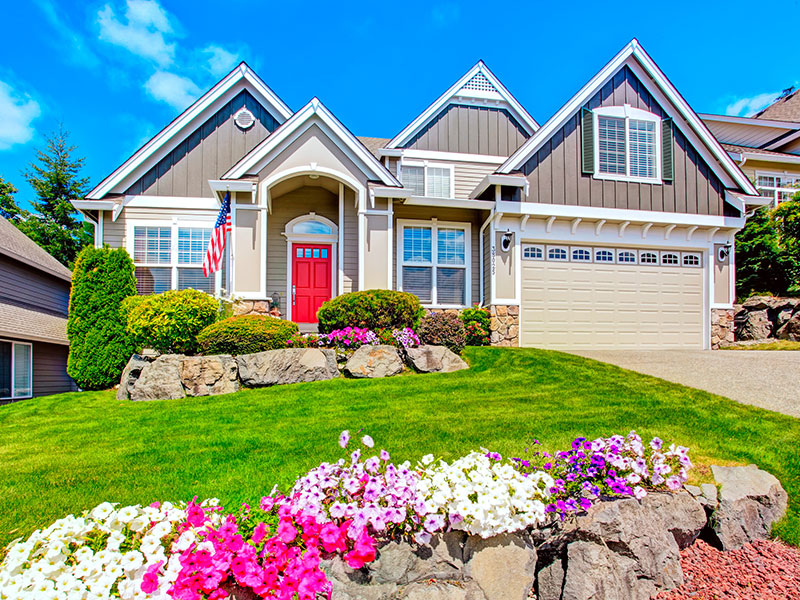 Photo of the front of a home with bright flowers and a bright green turf lawn